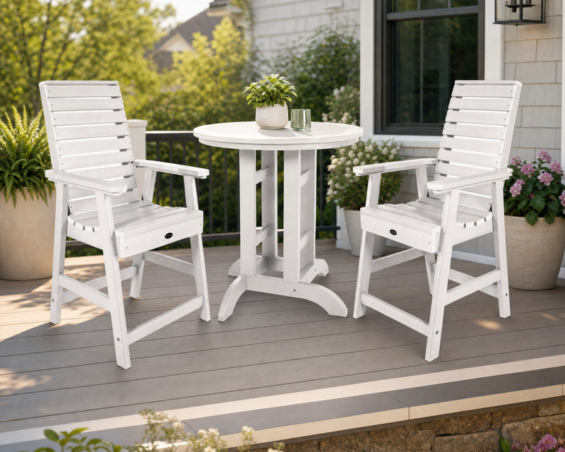 Sequoia white counter height table with 2 white counter height chairs on a wooden porch with potted plant and flowers.