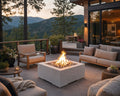 HPC 40-inch Alea lightweight concrete firepit with natural beach stones on a stone patio next to a mountain top home surrounded by comfortable seating, potted plants and flowers.  