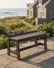 Brown  bench on a stone patio with ocean view and house in the background