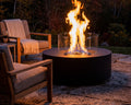 HPC 48 inch tempered glass guard on a fire pit placed on a stone patio with teak seating at dusk. 