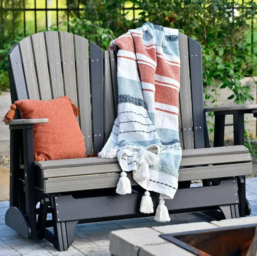 Gray glider with a striped blanket and orange pillow in an outdoor setting.