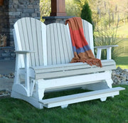 White glider with a colorful blanket draped over it, set against a stone wall and grassy area.