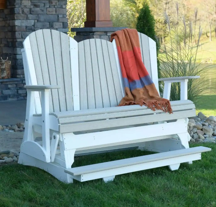 White glider with a colorful blanket draped over it, set against a stone wall and grassy area.
