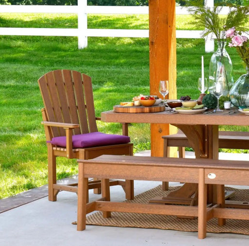 Outdoor patio furniture set including a Adirondack chair with a purple cushion, a matching dining table, and a bench on a concrete deck with a grassy lawn in the background.