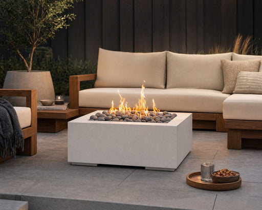 HPC Alea 32-inch lightweight concrete firepit with slate beach stones and flames centered in a teak seating area on a stone patio.  