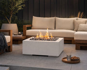 HPC Alea 32-inch lightweight concrete firepit with slate beach stones and flames centered in a teak seating area on a stone patio.  