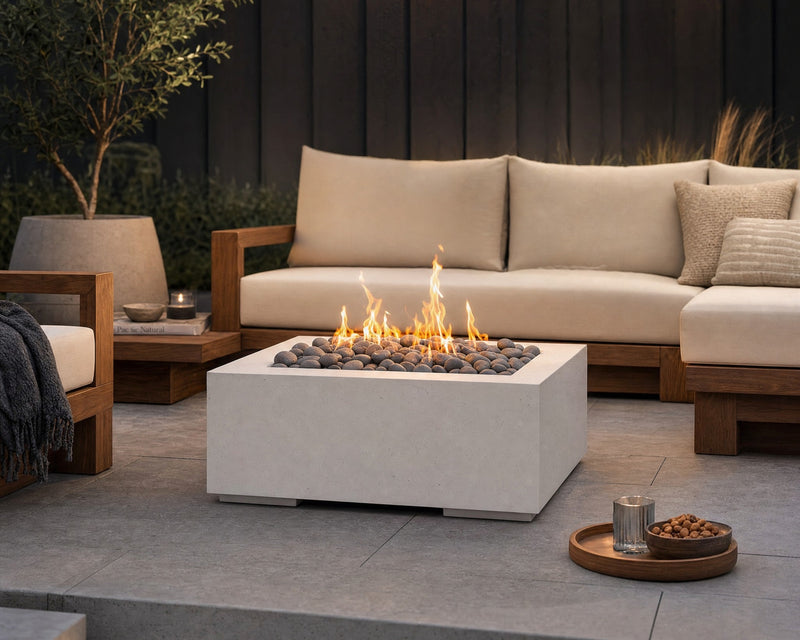 HPC Alea 32-inch lightweight concrete firepit with slate beach stones and flames centered in a teak seating area on a stone patio.  