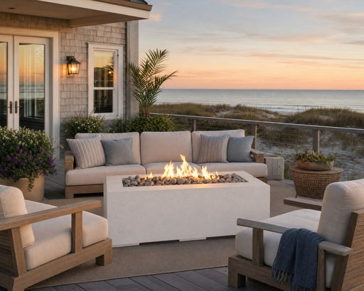 Avera 48-inch natural concrete fire pit placed in the middle of a teak seating arrangement on a wooden patio with ocean views. 