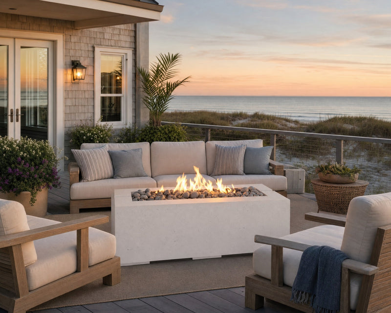 Avera 48-inch natural concrete fire pit placed in the middle of a teak seating arrangement on a wooden patio with ocean views. 