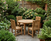 Anderson Teak Bahama 42 inch round table with four Chelsea Dinging Chairs on a stone patio in a private courtyard with shrubs and flowers.  