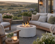 Belmont natural concrete fire pit with ivory beach stone centered amongst a teak seating area on a stone patio with rural views.  
