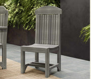A gray outdoor dining chair with a tall slatted back, shown on a patio with a dark wall and greenery in the background.