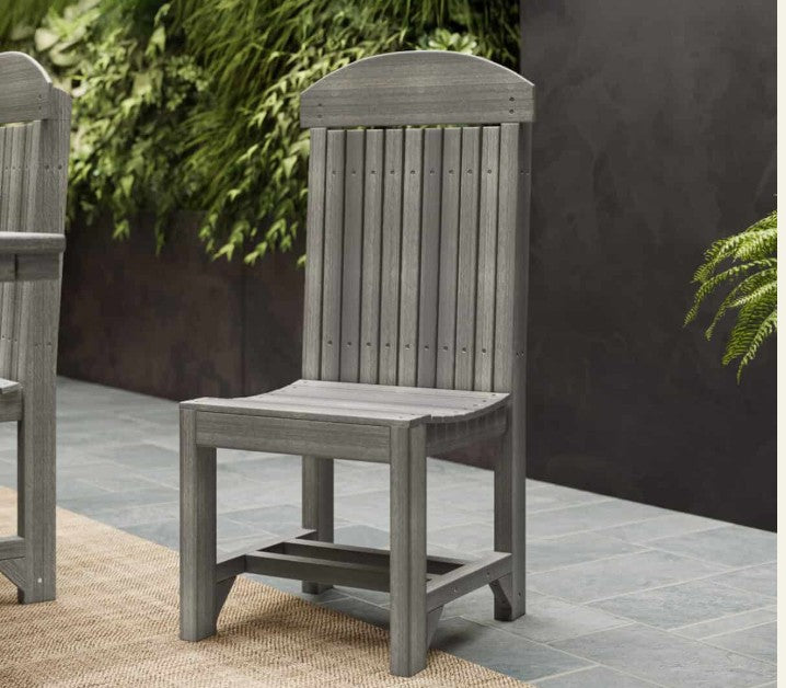 A gray outdoor dining chair with a tall slatted back, shown on a patio with a dark wall and greenery in the background.