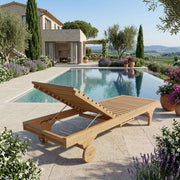 Anderson Teak Capri Sun Lounger with backrest raised, showing built-in wheels and slatted teak construction beside a resort-style pool