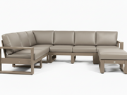 A modern outdoor sectional sofa set with a left-facing armchair, a curved three-seat section, a right-facing chaise ottoman, and a matching side table, all in a taupe-beige leather-like material with a weathered taupe frame, shown on a white background.