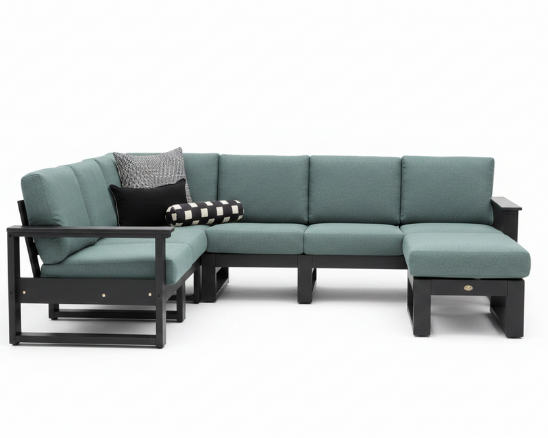 An outdoor sectional sofa set with a left-facing chaise lounge, a three-seat section, and a right-facing ottoman, upholstered in a muted teal fabric with a dark charcoal frame. Two decorative throw pillows are placed on the left side: one solid black and one black and white checkered.