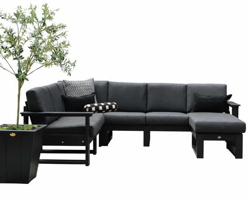 A modern outdoor sectional sofa set in dark charcoal gray with black wooden frames, including a chaise lounge, matching ottoman, side table, and black-and-white patterned accent pillows, shown against a plain white background with a potted tree on the left.