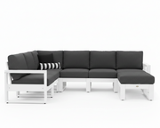 A modern outdoor sectional sofa with a white frame and dark gray cushions, including a chaise lounge on the right and a striped accent pillow on the left, shown against a plain white background.
