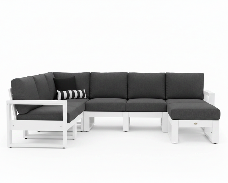 A modern outdoor sectional sofa with a white frame and dark gray cushions, including a chaise lounge on the right and a striped accent pillow on the left, shown against a plain white background.