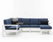 A modern outdoor sectional sofa with a white frame and navy blue cushions, styled with black and patterned accent pillows on a seamless white background.