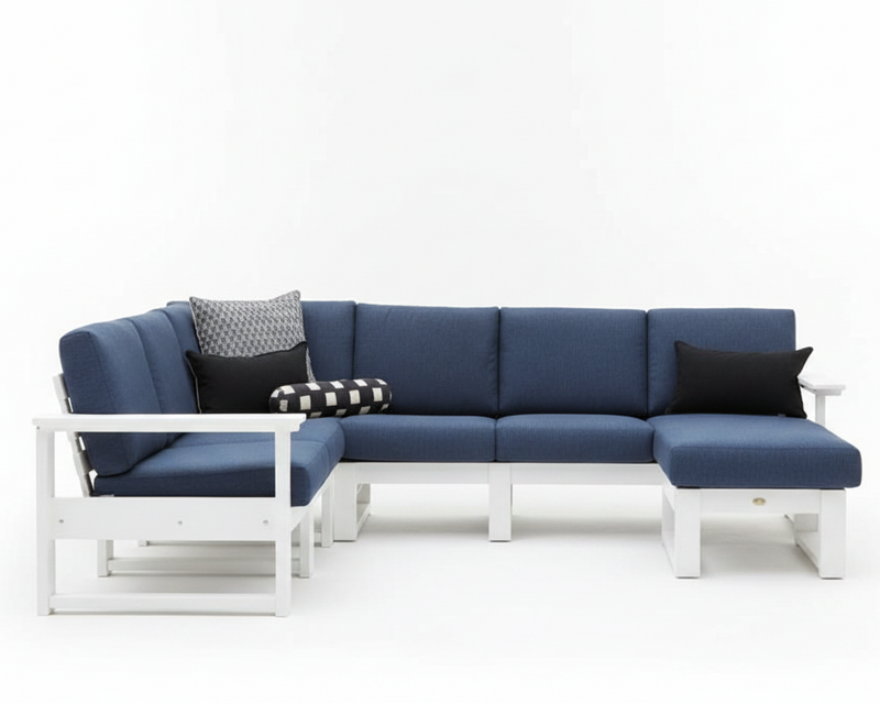 A modern outdoor sectional sofa with a white frame and navy blue cushions, styled with black and patterned accent pillows on a seamless white background.
