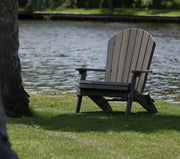Gray folding Adirondack Chair near a lake on a patch of grass.  