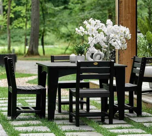 A black outdoor dining set consisting of a rectangular table and four matching chairs, styled with white flowers on a stone patio in a garden setting.
