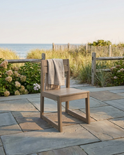 chair with a towel draped over it on a stone patio with a beach view.