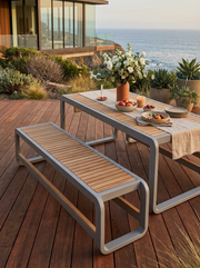 Anderson Teak Monza 3-seater bench and dining table on a wooden patio near the ocean. 