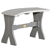 A gray outdoor bench with a curved seat and textured legs, featuring a small gold circular emblem on the center support beam, shown against a plain white background.