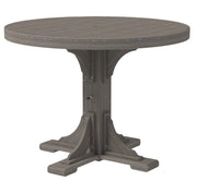 A round outdoor dining table with a weathered gray wood-look finish, featuring a central pedestal base with decorative bracket details and small metal rivets around the tabletop edge.