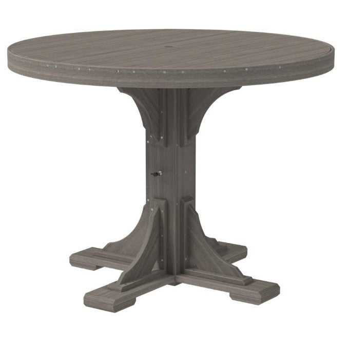 A round outdoor dining table with a weathered gray wood-look finish, featuring a central pedestal base with decorative bracket details and small metal rivets around the tabletop edge.