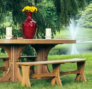 Outdoor picnic table and matching benches on a grassy lawn, with a red vase of yellow flowers and white candles on the tabletop, set against a pond with a fountain and trees.