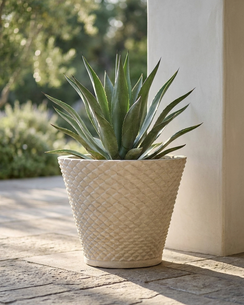 Limestone planter with a woven pattern on a stone patio next to a column with an aloe vera plant.  