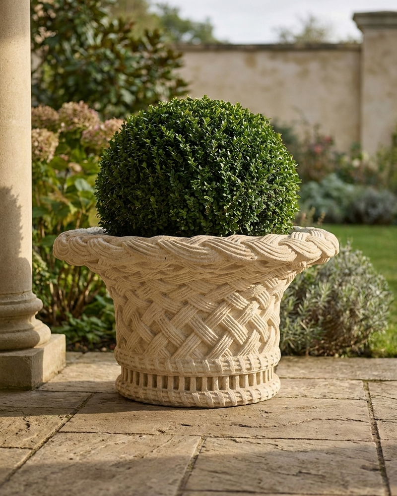 A Limestone planter with a lush  plant on a stone patio near a stone column.