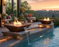 HPC Sedona 40-inch hammered copper fire and water bowls nesting beside an inground pool on a stone patio with a seating area and soft lighting.  