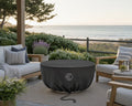 HPC Serenade fire pit covered with a vinyl cover while set on a stone patio and seating area with beach views.  