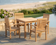 Wooden outdoor dining set with four chairs on a patio by a pool.
