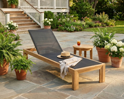 Smyrna teak sun lounger on a stone patio .
