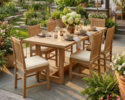 Smyrna Dining Table in teak with 6 Saratoga dining chairs with natural-colored cushions.  Dining set is on a stone patio in a backyard. 
