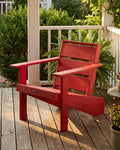 Red Adirondack chair on a wooden deck with greenery in the background