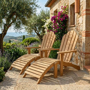 Two Aderson Teak Adirondack chairs with Ottomans on a stone patio next to a stone house with lush gardens and flowering vines. 