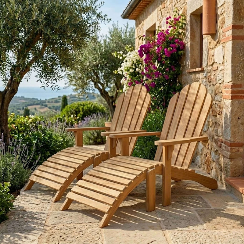 Two Aderson Teak Adirondack chairs with Ottomans on a stone patio next to a stone house with lush gardens and flowering vines. 