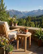 Outdoor patio furniture set with a light wood armchair and matching side table on a stone deck, decorated with potted flowers and ferns, overlooking a lush mountain forest landscape.