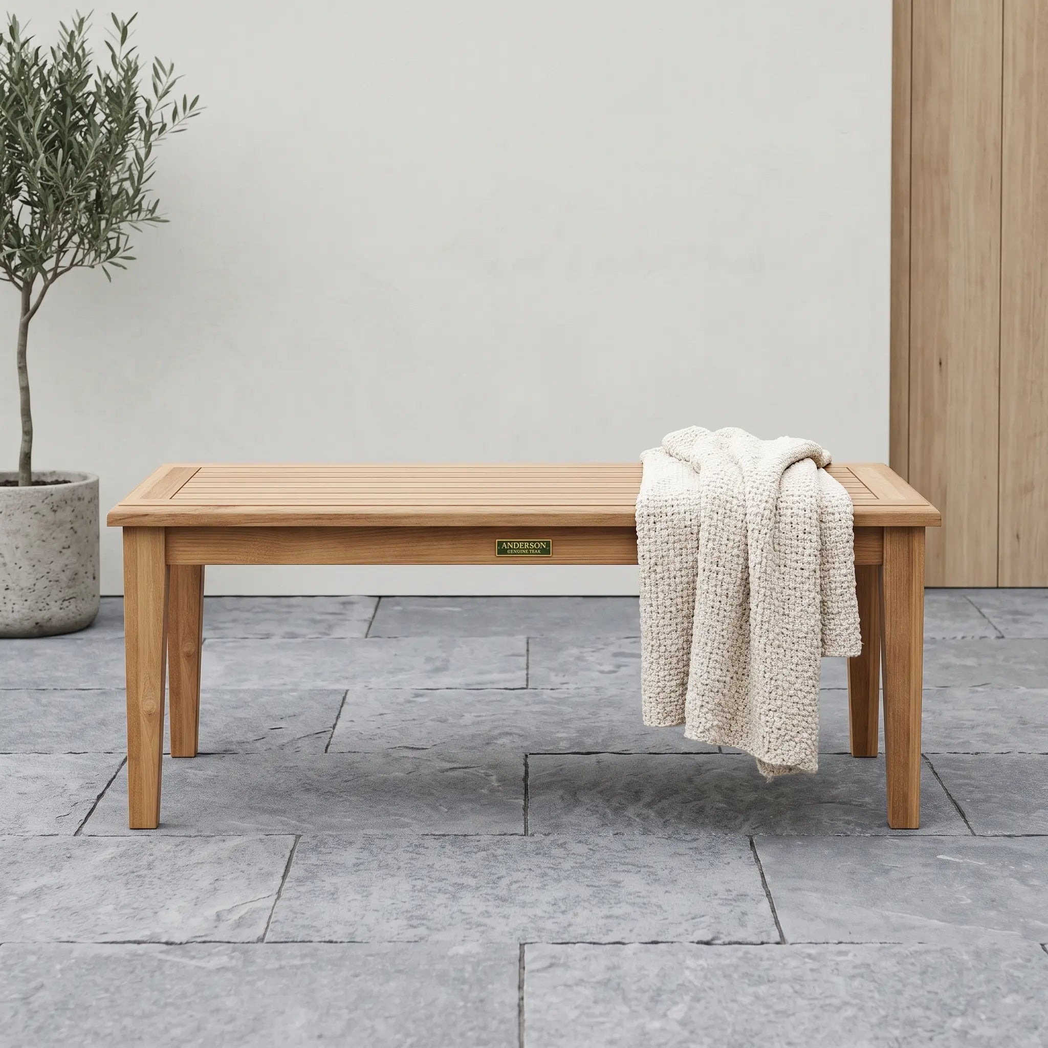 Teak rectangular coffee table on a stone patio with a sweater on it.  