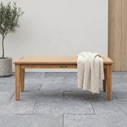 Teak rectangular coffee table on a stone patio with a sweater on it.  