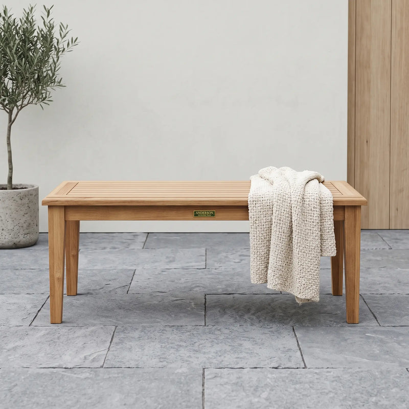 Teak rectangular coffee table on a stone patio with a sweater on it.  