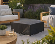 HPC vinyl fire pit cover for the Alea 32 and bravo units on a fire pit on a stone patio centered amongst teak seating, potted plants and flowers.  