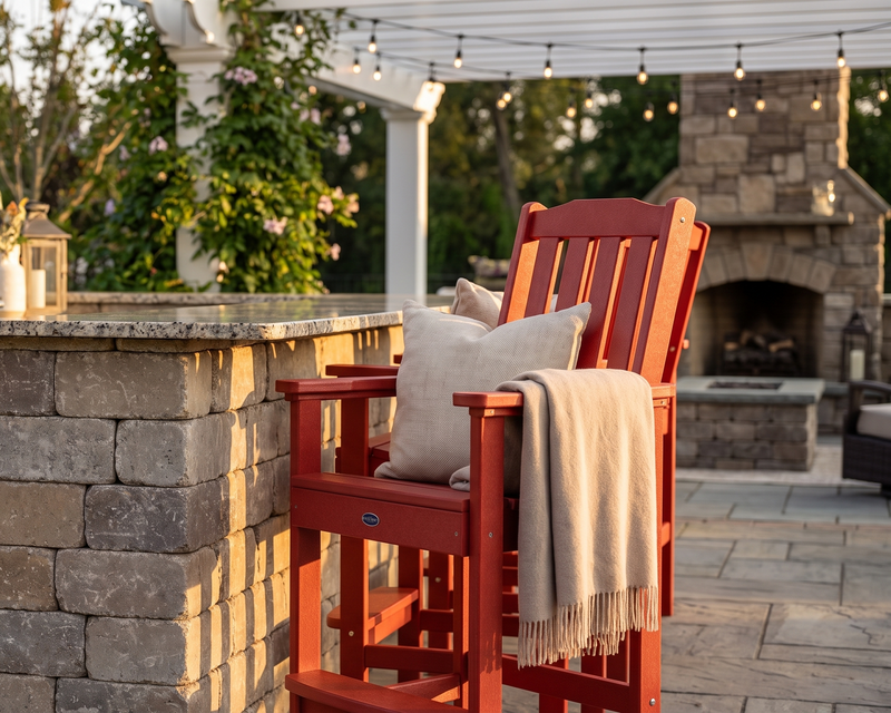 Red outdoor chair with a beige blanket and pillow on a patio with stone wall and fireplace.