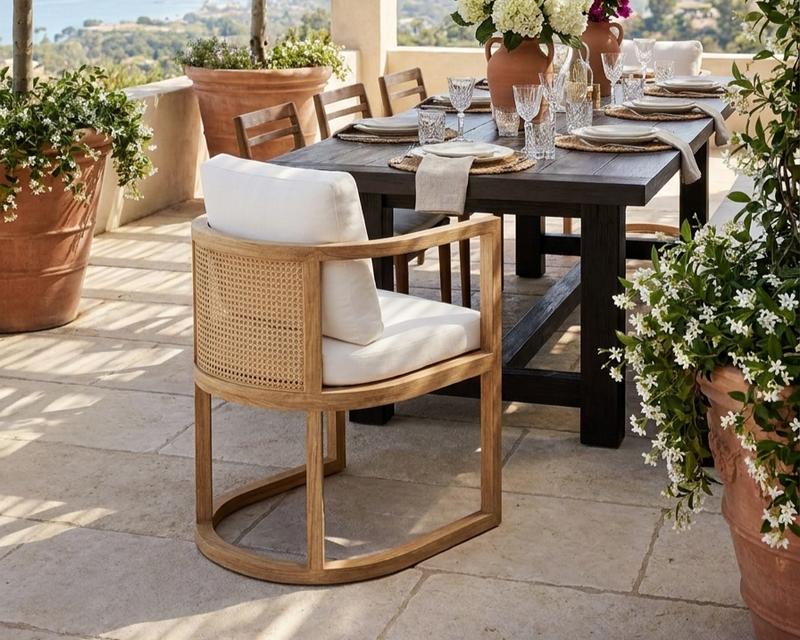 Anderson teak junus dining armchair with natural cushion featured on a stone patio with a dark wooden table  set for dinner.  Dining table is surrounded by large terra cotta pots with draping white flowers.  